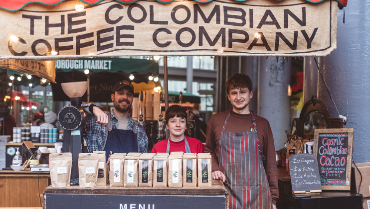 Three baristas smile behind the Colombian Coffee Co. stall at Borough Market