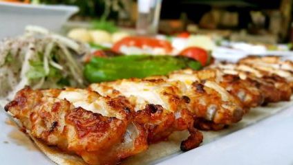 A row of griddled chicken breast stuffed on flat bread and green peppers, tomatoes at the side