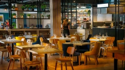 Inside the restaurant, wooden chairs and tables with wine glasses and an open kitchen