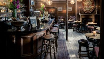 Inside the Holly Bush pub, Hampstead London. A large wooden bar with lots of round wooden tables and chairs