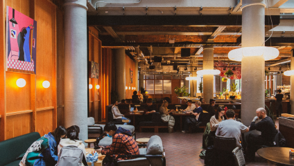 Inside the lounge - people sitting on seats and sofas underneath grey industrial pipework.