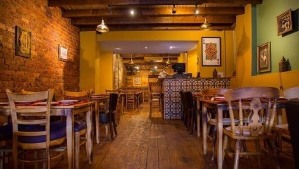 Inside the restaurant with yellow walls, wooden table and chairs, green walls and ornate tiles