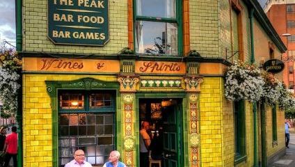 yellow tiles and green windows. 2 men sitting outside on a bench drinking pints.