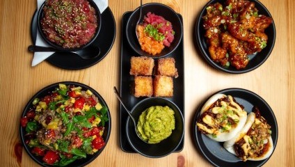 5 black plates and bowls containing multi coloured sushi and starters