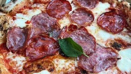 Close-up of a pizza with red tomato sauce and salami and single basil leaf on top