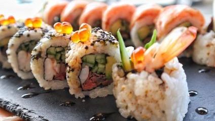 A row of sushi rolls with rice and a mix of fish and colourful veggies inside