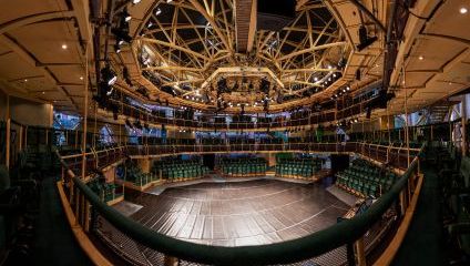 Inside the an old Corn Exchange is a metal scaffold built round theatre. Rows of green seats, a stage and many lights over the main stage