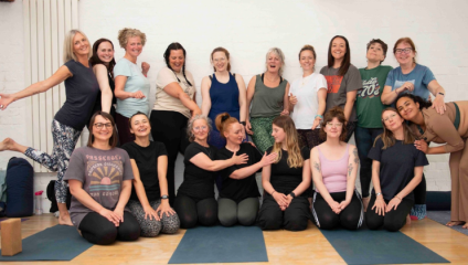 A large group of yoga enthusiasts at The Bristol School of Yoga line up against the wall of the studio for a photo, smiling