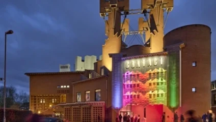 Turreted castle shaped building with lit up in the dark with red, yellow, green and blue lights at the front