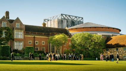 Glyndebourne Opera House; an assortment of opera enthusiasts mingle on the lawn outside Glyndebourne's historic house. To the right of the historic house is Glyndebourne's impressive round theatre building