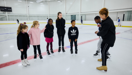 A group of children are lined up listening to their skating instructor on the ice rink at Lee Valley Ie Centre