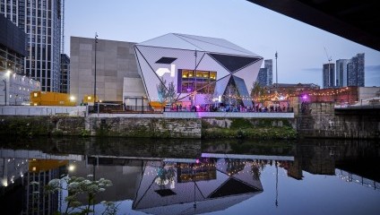 Outside the Factory International white and concrete space reflecting in the water and people standing outside it