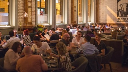 Lots of people at the restaurant eating and drinking. Large Victorian windows and white tiles on the wall.