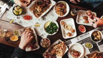 Lots of mexican food on a table and people's hands spooning from the bowls