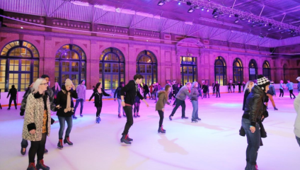 Skaters on the ice rink set within the grand setting of Alexandra Palace, bathed in a purple light