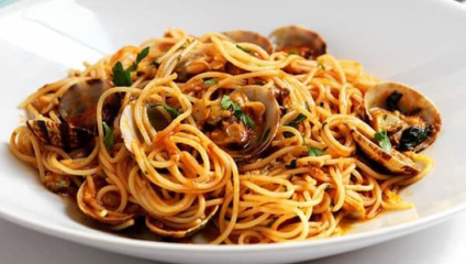 A white plate filled with spaghetti and clams, covered in a rich tomato-based sauce. The dish is garnished with fresh parsley. The clams are open, revealing their tender meat, and the pasta is cooked to al dente, intertwining with the sauce and seafood.