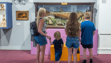 Inside Salford art gallery. Family of 4 standing viewing a large fish in a glass frame