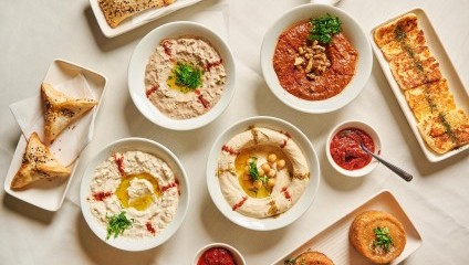 red and white starters in white bowls, triangle puffs, fried hallumi and red sauce on a white tablecloth