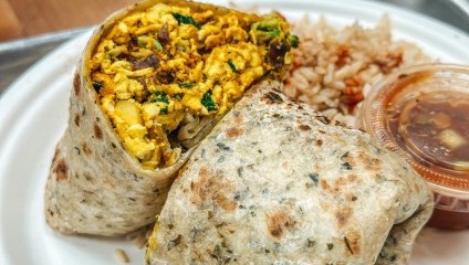 A burrito packed with chicken and side of rice and sauce