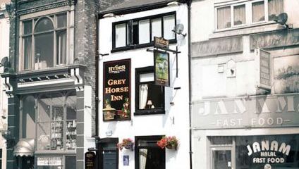 Outside shot of the front of the Grey horse pub. small, white with black window frames and a large black oblong sign