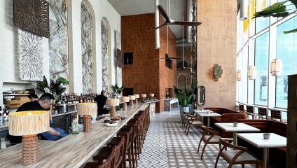 inside the Kitten restaurant. Long bar, white marble tables, wooden chairs  and large tropical green plant