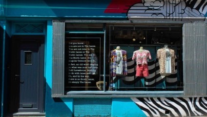 A shop display seen from the street where several vintage dresses can be seen through the large glass window