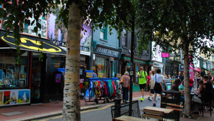 Leafy section of Sydney Street, Dave’s Comic’s in the foreground, Dirty Harry’s outdoor clothes rails central.