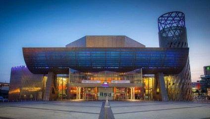 Image of the front of the Lowry arts centre - made of grey concrete with the lights on inside