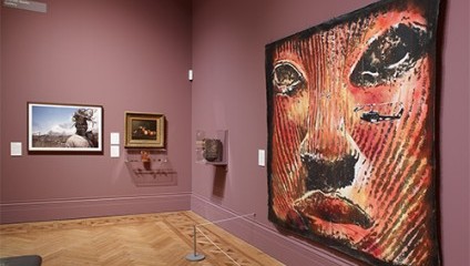 2 dark pink walls inside the Manchester art gallery focusing on one large painting of a red and yellow face and smaller painting in the background.