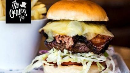 Large meat burger with lots of cheese, lettuce and a skewer holding it together. Chips in a white bucket at the side.