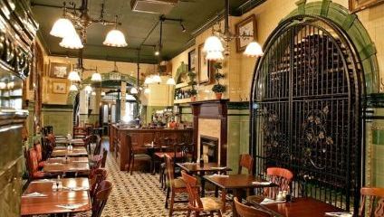 Inside the Victorian pub, wooden tables, tiles on the floor, green walls and low hanging lights