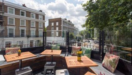 The Queens pub roof terrace with square wooden tables and chairs overlooking Primrose Hill high street in the sunshine.