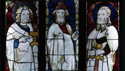 Stained glass art depicting three historical or religious figures, each holding a distinct object. The left figure holds a chalice, the middle one holds a scroll, and the right one holds a sword. The background features ornate, colorful designs.