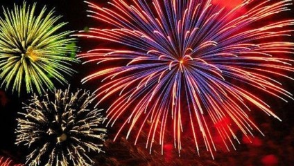 Vibrant fireworks burst against the night sky in a display of colors. Red, blue, green, and yellow explosions of light fill the image, creating a festive and celebratory atmosphere. The bright hues and varying patterns highlight the beauty of the fireworks.