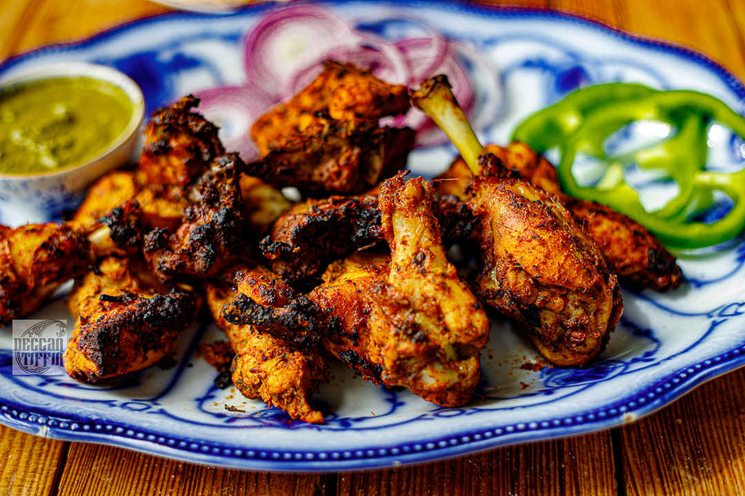 Delicious plate of marinated fried chicken with raw pepper and onion and a green dip. High quality close up shot on a blue and white china plate on a wooden table.