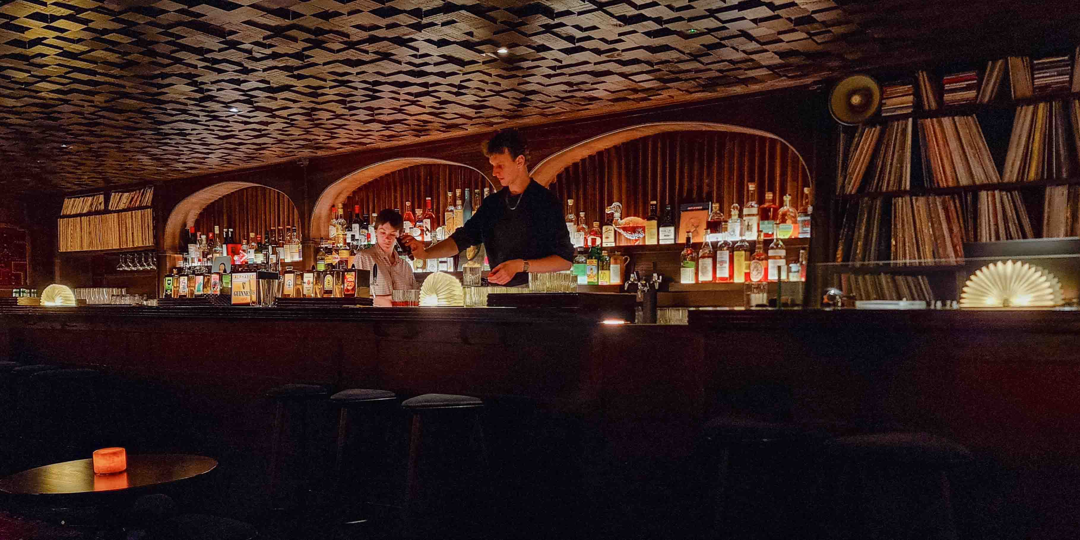 Two mixologists prepare cocktails in gorgeous, lamp-lit, speak-easy style bar.