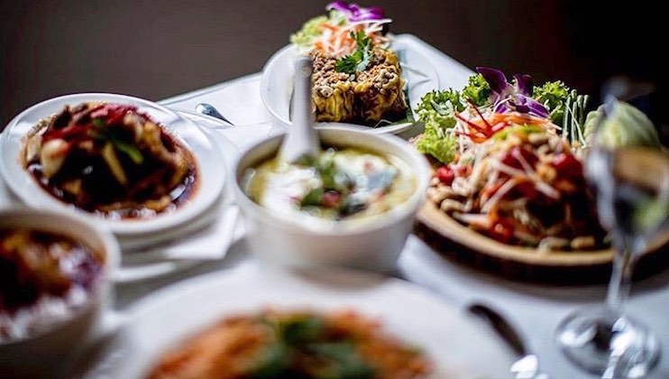 A table is set with a variety of colorful dishes, including salads, a dish served in a hollowed pineapple, and bowls of what appears to be soups and stir-fries. The presentation is elegant, with garnishes like lettuce, carrots, and purple cabbage adding vibrant touches.