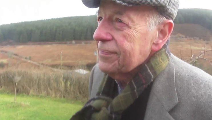 Writer Christopher Burn, author of Poetry Changes Lives, is wrapped up warm and wearing as flat cap as he looks wistfully into the distance in a lush green countryside setting