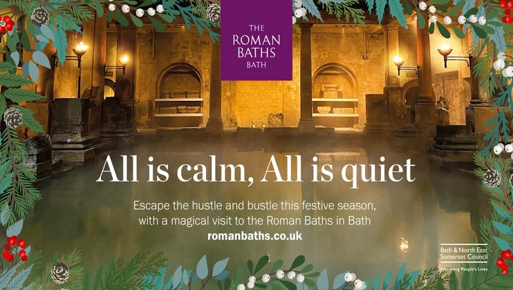 A serene nighttime image of the Roman Baths in Bath, decorated with festive holiday greenery. Text reads, All is calm, All is quiet. Escape the hustle and bustle this festive season, with a magical visit to the Roman Baths in Bath. romanbaths.co.uk.