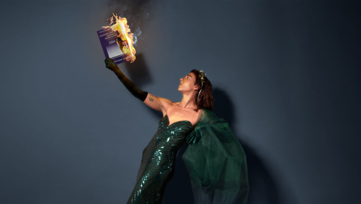 Wearing an green ball gown, Sammy Trotman holds aloft a burning copy of the DSM