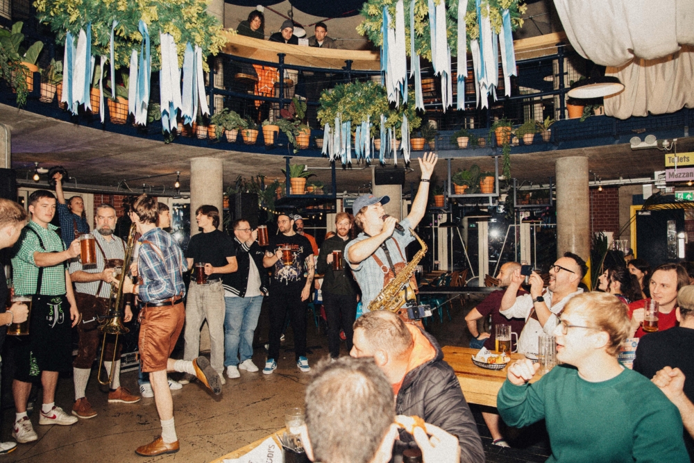 A packed party atmosphere at Oktoberfest. A musician takes centre stage surrounded by onlookers drinking steins.