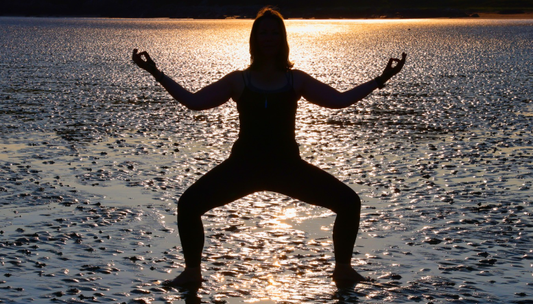 A silhouetted woman holding a yoga pose on Brighton beach at dusk.