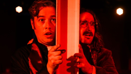 Bathed in a blood-red light, Alex Knott and James Demaine clutch either side of a pillar and look outwards, terrified in character as (respectively) Bishop Patrick Sheffield and Daniel Farringdon in their play The Highgate Vampire