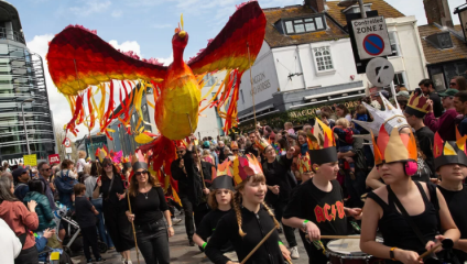 Th Children's Parade at Brighton Festival; hundreds of children dressed in black march and beat drums as a giant papier mache phoenix follows them through the streets of Brighton.