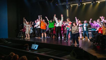 Group of performers on stage raising their arms at end of performance - Theatre Trust
