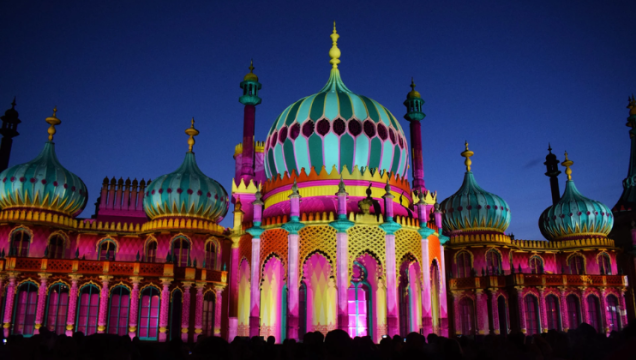 The magnificent Brighton Dome at night, illuminated in yellows, greens, reds and pinks. One of our top picks from our what's on in Brighton guide.