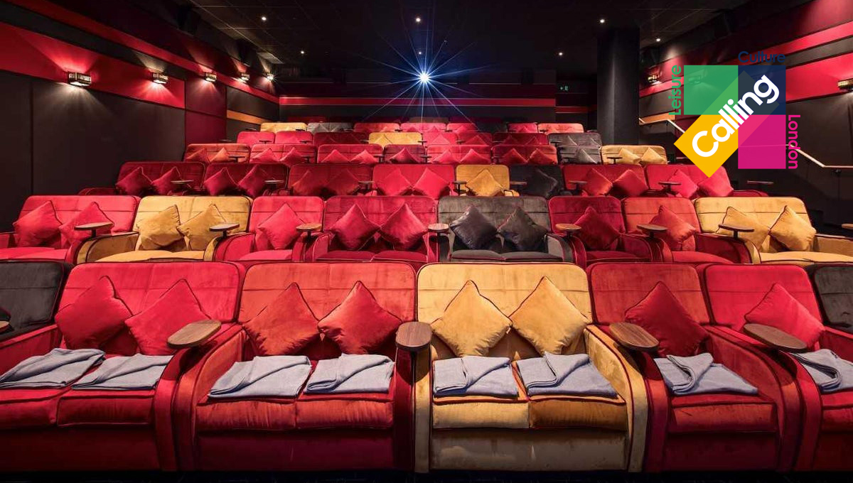 A cozy, modern cinema features plush red and yellow seating with cushions and neatly placed blankets. The screen area displays vibrant colors along with the text London Calling in a playful, diagonal arrangement.