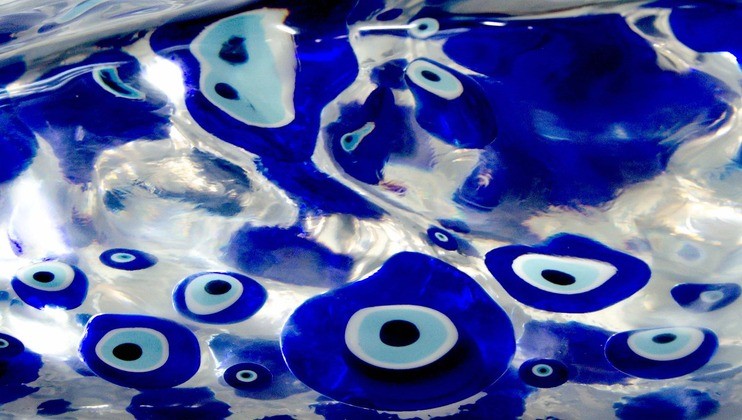 A close-up photograph showing abstract white and blue shapes that resemble eyes with concentric circles. The shapes are set against a reflective, smooth surface, creating an illusion of depth and fluidity. The overall color palette is blue and white.