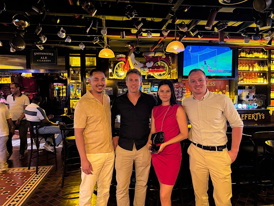 A group of previous stangers stand smiling in a bar after enjoying a restaurant of the week event - a micro-event where a small group of strangers meet up for a meal at a restaurant.