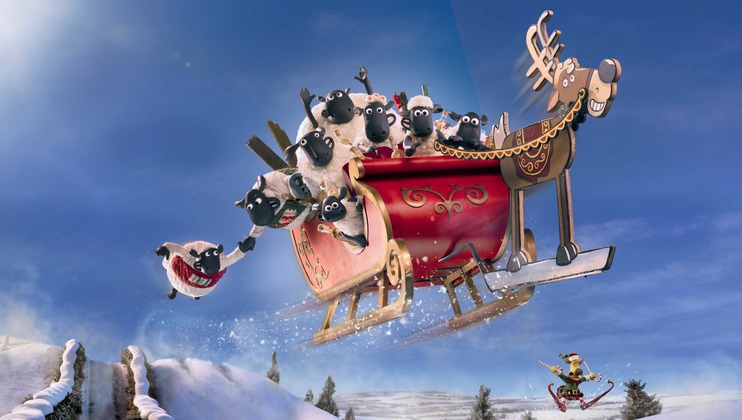 A group of animated sheep are joyfully riding in a red sleigh pulled by a reindeer, soaring through a snowy landscape. One sheep is hanging off the side, while another looks on from a smaller sled below. The sky is bright and clear, adding to the festive scene.